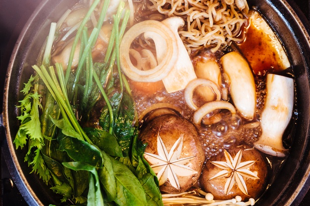Close up top view of sukiyaki hot pot with boiling vegetables including cabbage, konjac noodle, onion, carrot, shiitake, enokitake and tofu in shoyu sauce soup. Premium Photo
