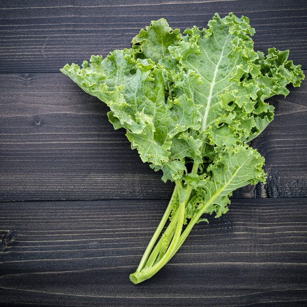 Fresh organic curly kale leaves flat lay on a wooden table with copy space. Premium Photo